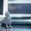 Toy robot in front of a monitor showing the security concerns over the chrome extensions used by checkout bots to snap up delivery time slots.