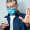 Man in mask using mobile showing how surveillance technology companies are selling spy tools as coronavirus contact tracers