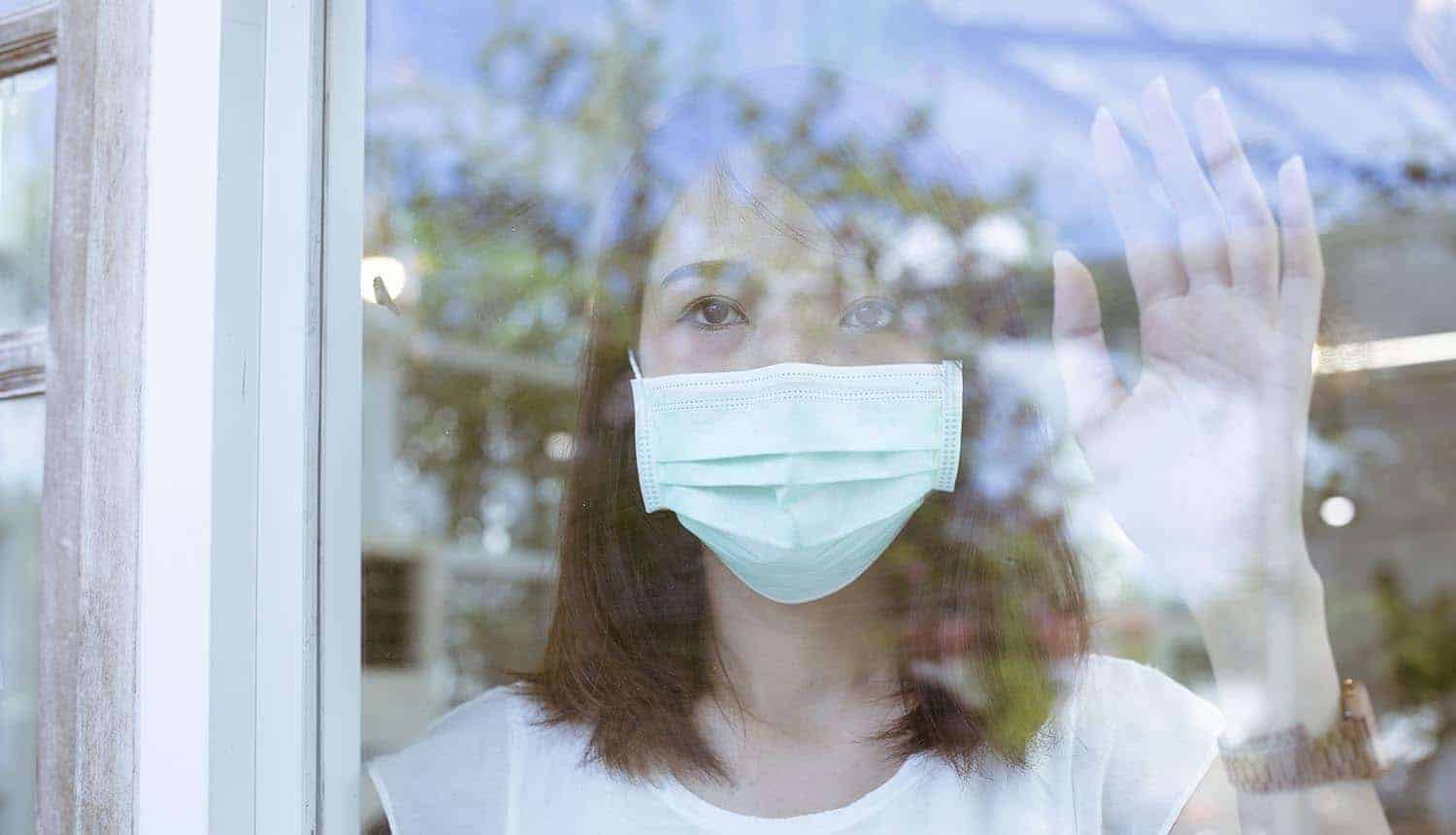 Woman in mask standing behind a window showing the new contact tracing wearable for COVID-19 tracking in Singapore