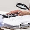 Close-up of a businesswoman examining accounts with magnifying glass showing cost of a data breach