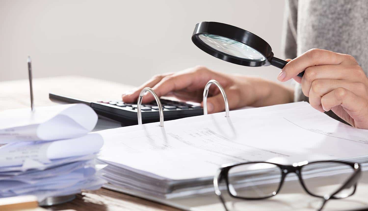 Close-up of a businesswoman examining accounts with magnifying glass showing cost of a data breach