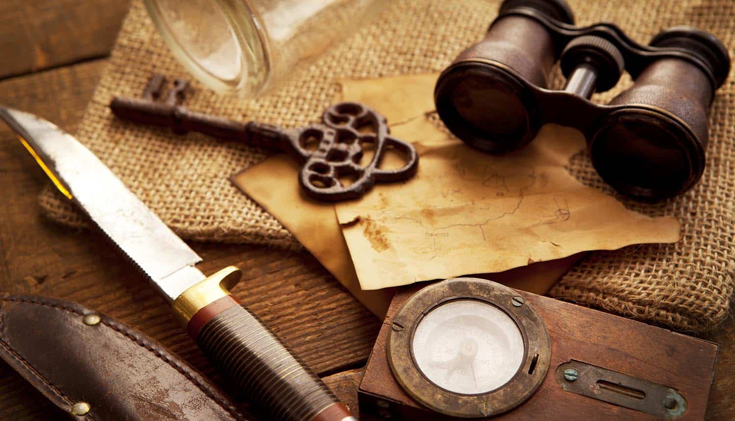 A compass, binoculars, knife and a old key on a old wooden desk