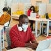 Male office manager in casualwear and protective mask using laptop showing workplace safety during pandemic
