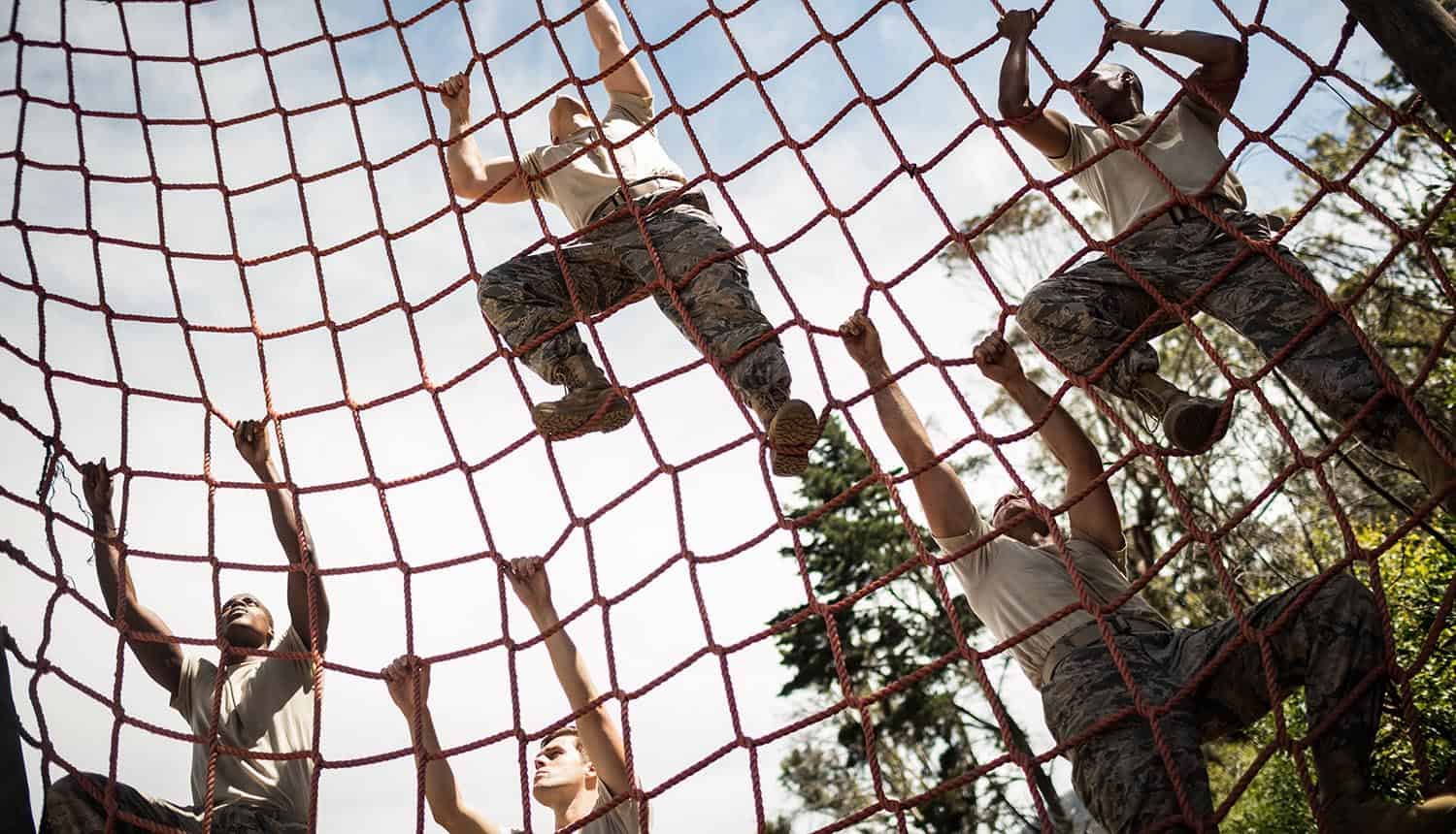 Military soldiers climbing rope during obstacle course showing defense contractors problem with CMMC requirements