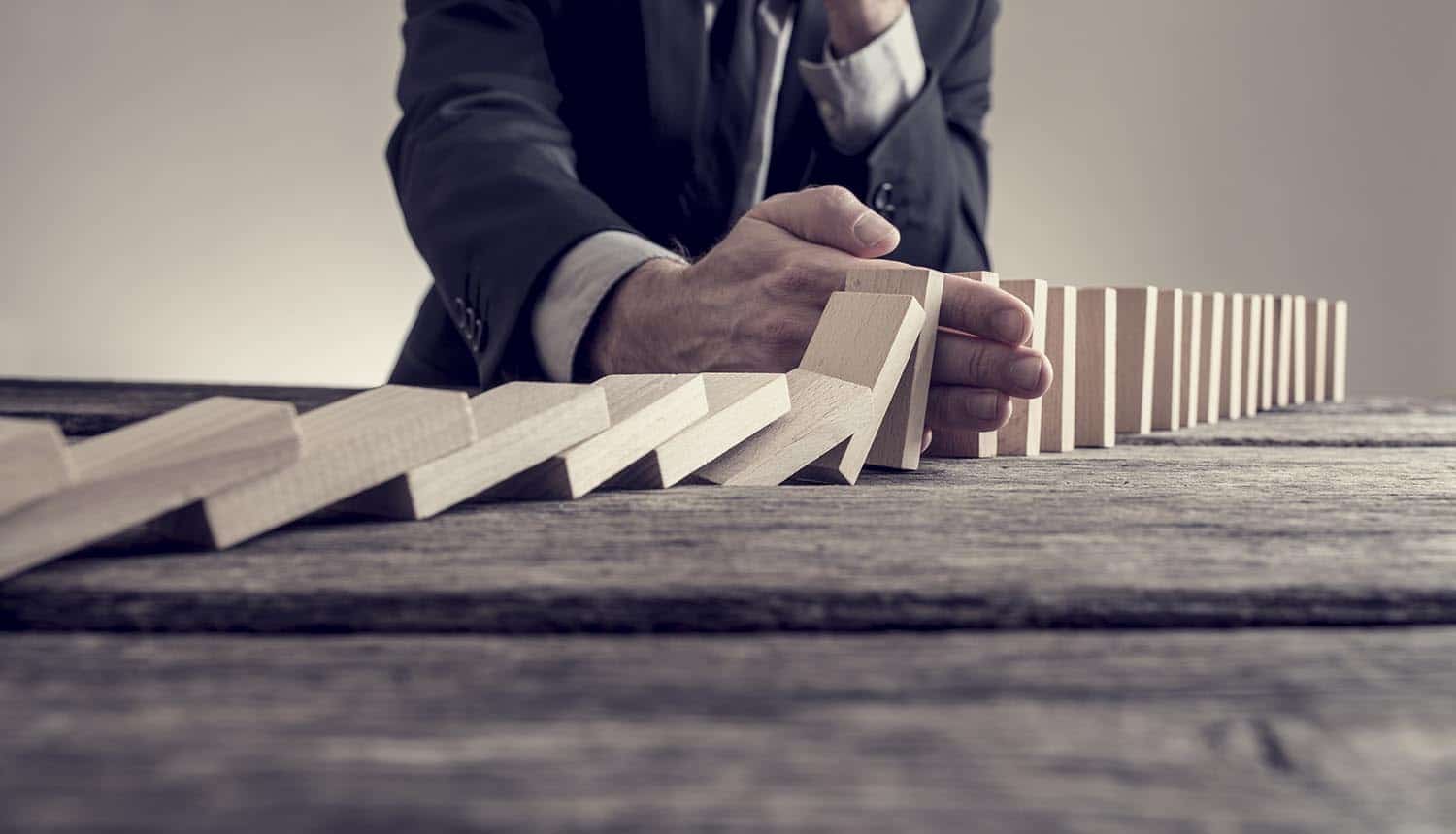 Businessman stopping domino effect on wooden table showing vendor risk management