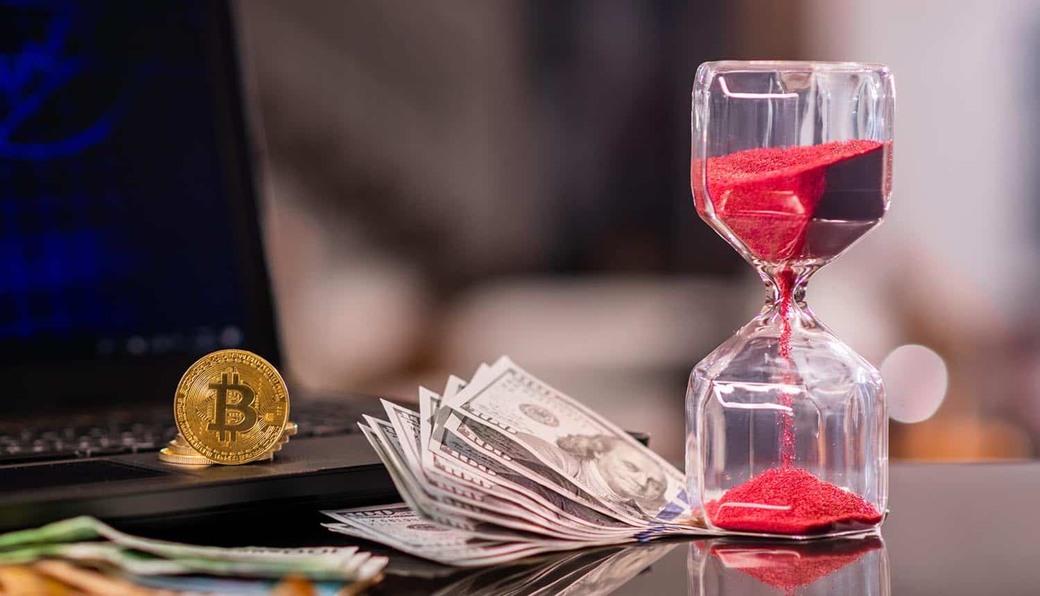 Hour glass and cryptocurrency in front of laptop showing ransomware payments