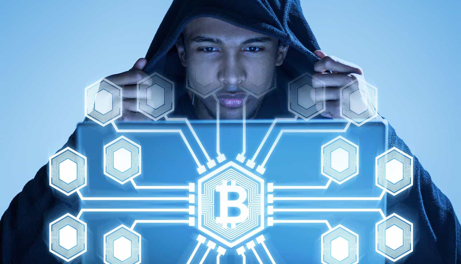 Hacker in a black hoodie looking at a glowing bitcoin