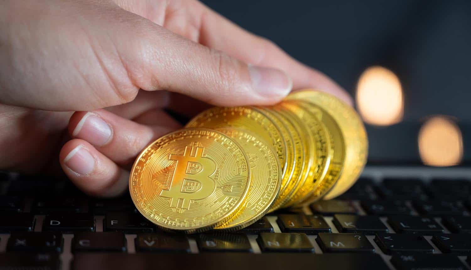 Close up of hand putting some pieces of golden Bitcoin token on laptop