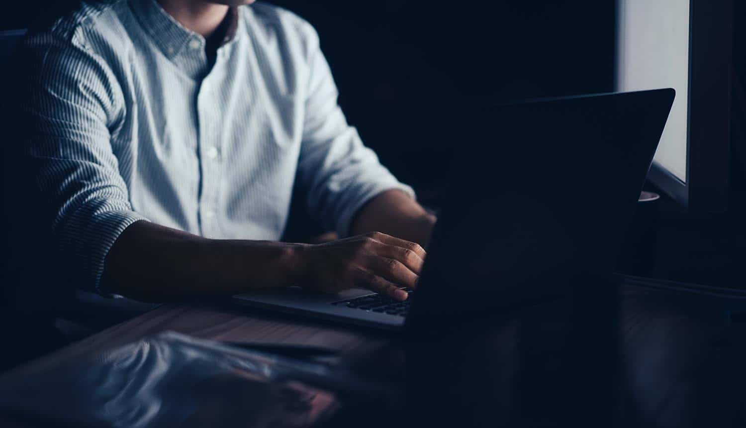 Employee working on a laptop late at night showing data breach of customer information