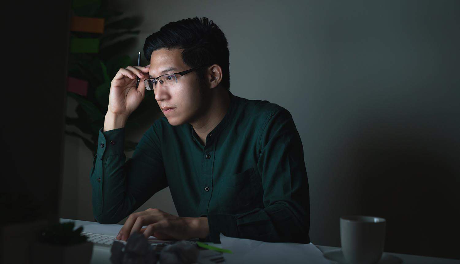 Young man looking at laptop computer in the dark showing Great Resignation increased risks of intellectual property theft