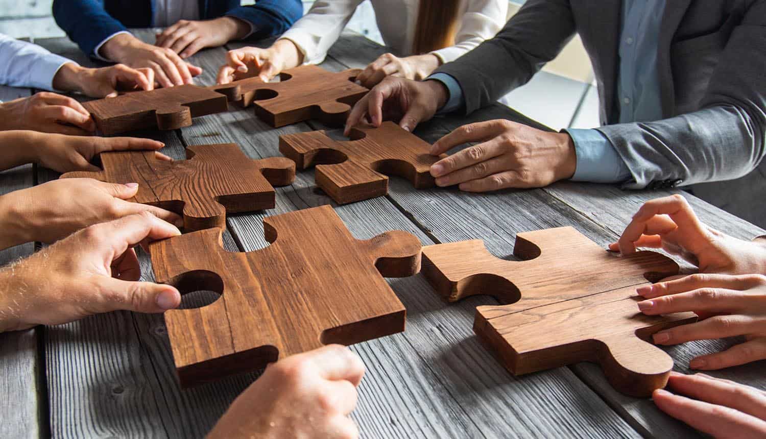 Business people sitting around meeting table and assembling wooden jigsaw puzzle fitting privacy in risk and compliance