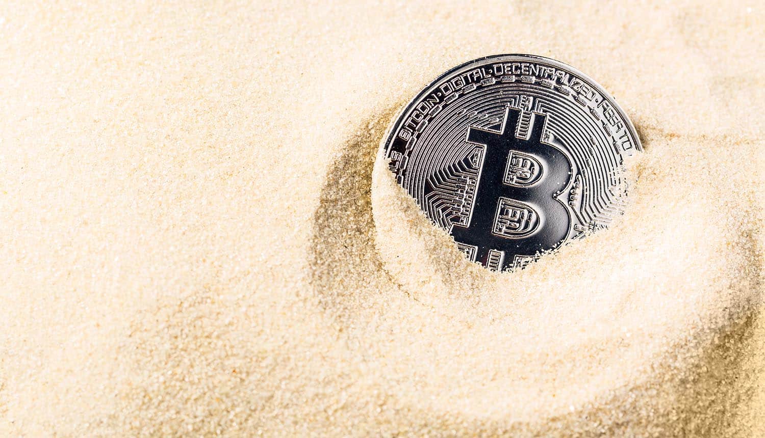 Bitcoin coin sinking in the sand