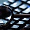 Magnifying glass on computer keyboard showing digital forensics and incident response for cyber insurance
