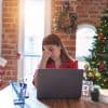 Woman sitting at the table working with laptop around Christmas tree showing phishing campaigns during holiday season