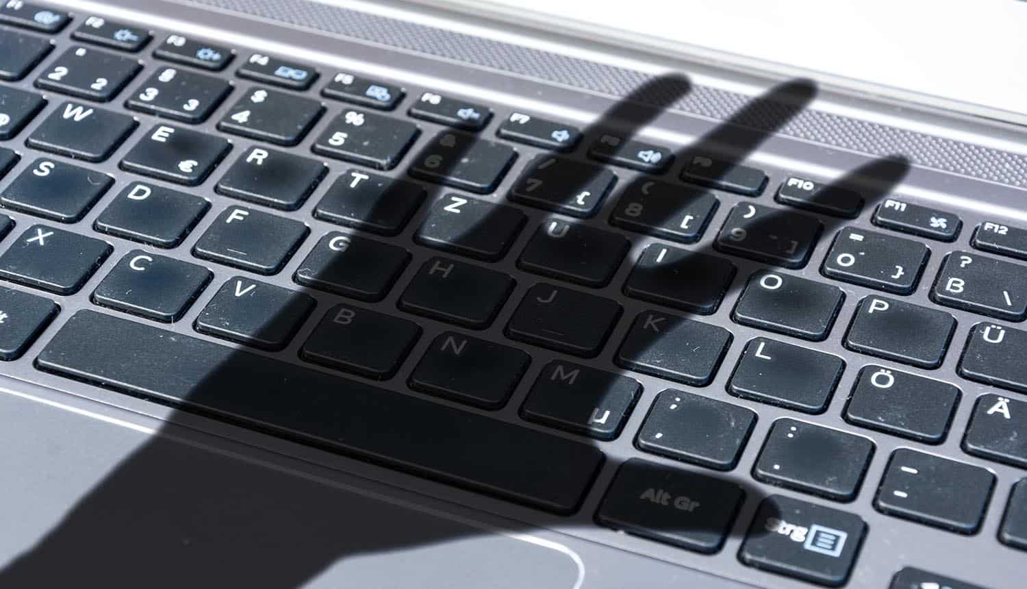 Dark shadow of a hand reaches for computer keyboard showing insider threat and user behavior