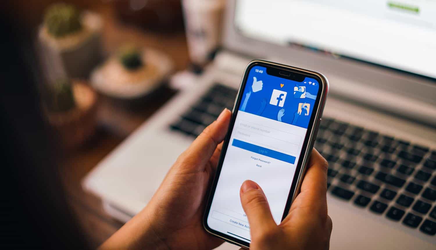Woman holding phone with Facebook on the screen showing Facebook Messenger phishing campaign