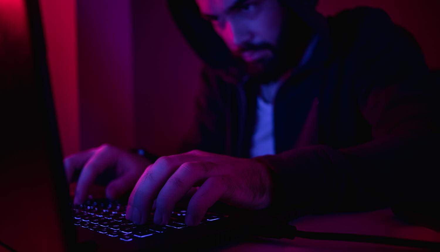 Man in hoodie typing on laptop showing data breach