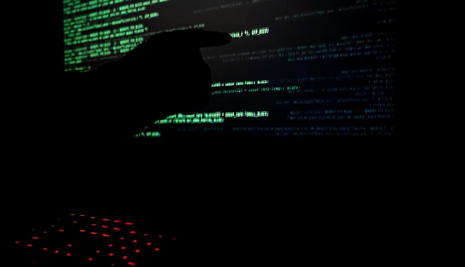 Hacker pointing to code on a monitor showing data breach and posted on dark web